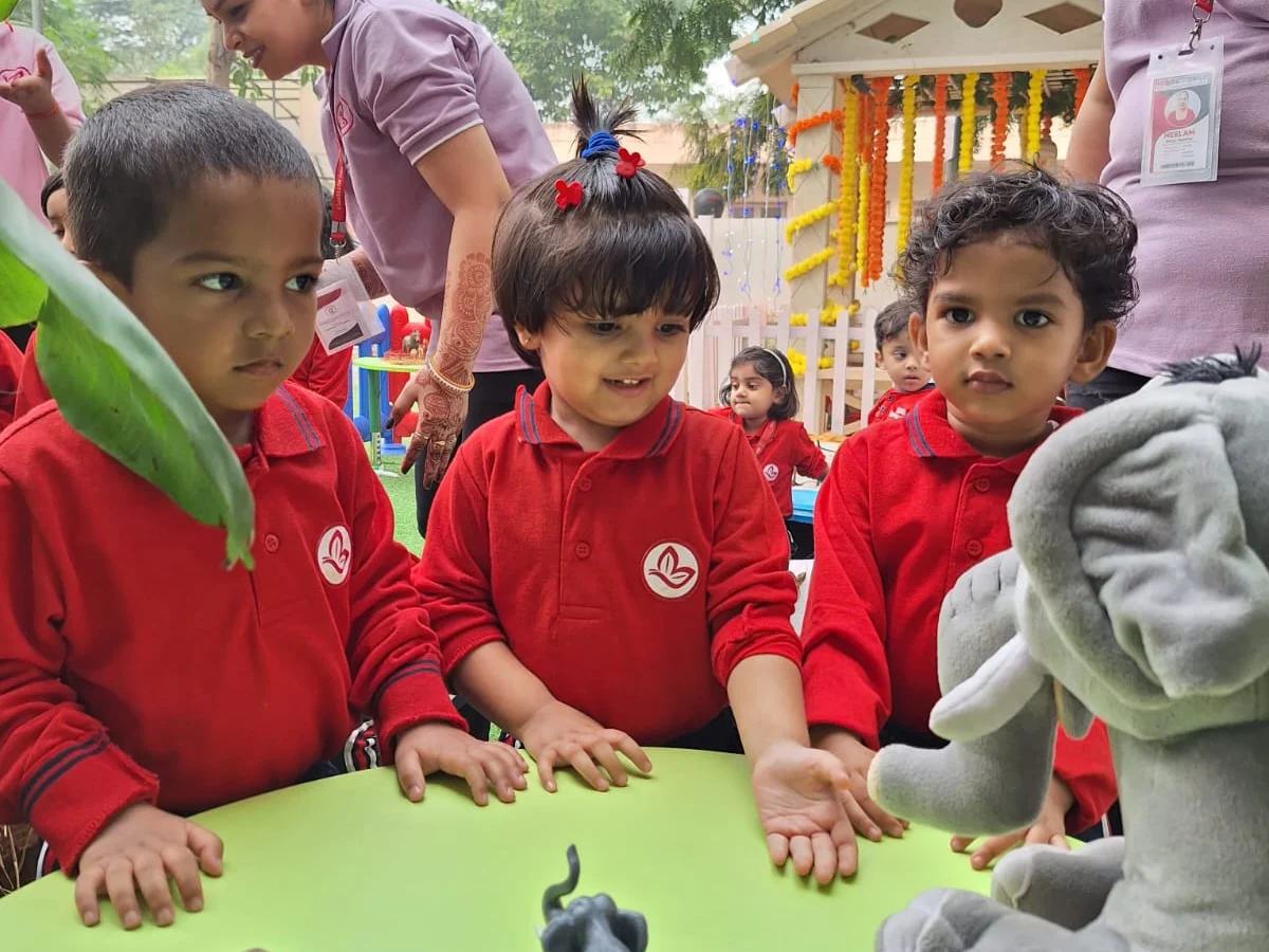 Pre Nursery toddlers gathered around a table exploring toy animals with their teacher