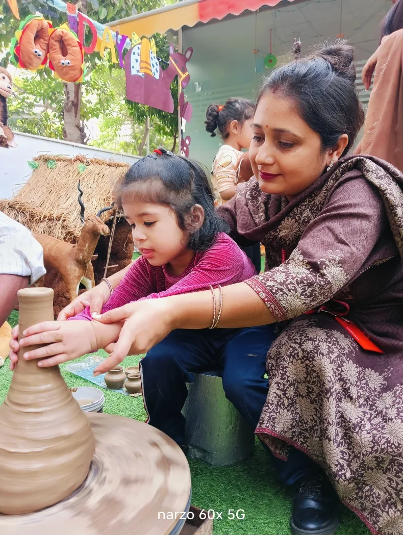 A teacher helping a child shape clay on a pottery wheel for Brown Day